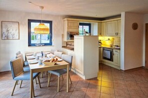 A dining area with a table set for four, a kitchen with white cabinets, and a window with a view. - Holiday home in Zingst with swimming pool (Zingst)