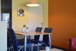 A dining area with a table, chairs, a clock, and a door. - Apartment with 1 bedroom (Hollum Ameland)