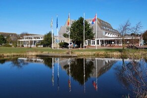 A building with a reflection in a calm body of water, surrounded by flags. - Apartment with 1 bedroom (Hollum Ameland)