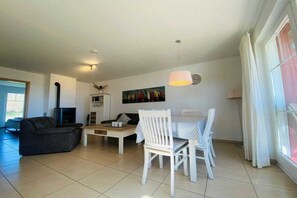 A living room with a sofa, a dining table with chairs, a fireplace, and a painting on the wall. - Holiday apartment with 2 bedrooms (Sierksdorf)