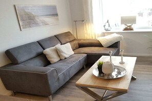 A modern living room with a grey sectional sofa, a wooden coffee table, and a decorative tray with candles. - Holiday apartment with 2 bedrooms (Grömitz)