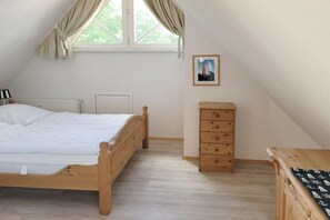 A bedroom with a wooden bed, a dresser, a radiator, and a window with curtains. - Aft deck W. 8 || Prerow (Prerow)