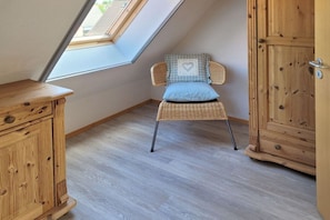 A room with a sloped ceiling, a wooden cabinet, a wicker chair with a heart-patterned cushion, and a wooden wardrobe. - Aft deck W. 8 || Prerow (Prerow)