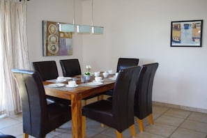 A dining area with a wooden table set for six, surrounded by black chairs, with a modern light fixture above and a framed artwork on the wall. - Holiday apartment with 2 bedrooms (Zinnowitz)
