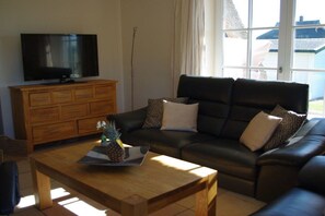 A living room with a wooden coffee table, a black leather sofa, a television on a wooden cabinet, and a window with curtains. - Holiday apartment with 2 bedrooms (Zinnowitz)