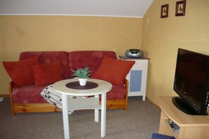 A compact living space with a red sofa, a small round table with a plant, a television on a stand, and a cabinet with a radio. - Holiday apartment with 1 bedroom (Wieck a Darss)