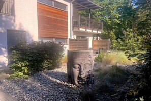 Ein modernes Gebäude mit Balkon, umgeben von einem Kiesweg und Grünflächen.
