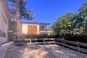 A modern building with a large garage door, surrounded by a wooden fence and trees. - Holiday apartment with 1 bedroom (Koserow)