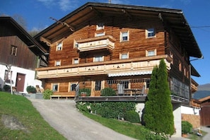 A traditional wooden chalet with a sloped roof, a balcony on the upper floor, and a paved driveway leading to the entrance. - Holiday apartment with 2 bedrooms (Zellberg)