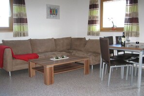 A living room with a sofa, a coffee table, and a dining area with chairs and a table. - Holiday apartment with 2 bedrooms (Zellberg)
