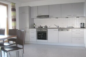 A modern kitchen with white cabinets, a built-in oven, a dishwasher, and a dining area with a table and chairs. - Holiday apartment with 2 bedrooms (Zellberg)