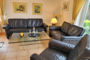 A living room with a glass coffee table, two black leather sofas, and three framed floral paintings on the wall. - Holiday home with 1 bedroom (Zinnowitz)