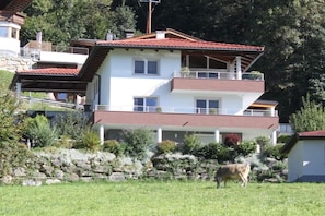 A two-story building with a red-tiled roof, a balcony on the upper floor, and a stone wall in the foreground. - Holiday apartment with 2 bedrooms (Ramsau im Zillertal)