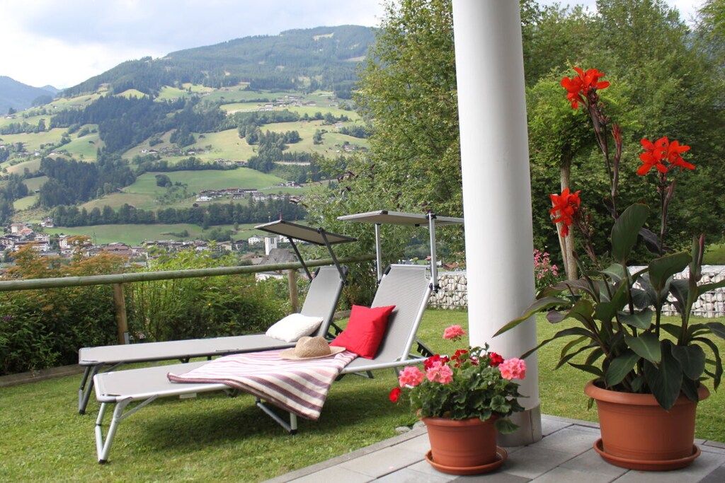 Une terrasse offrant une vue sur une vallée, une colonne blanche et deux fauteuils avec des coussins.