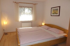 A single-bed room with a wooden headboard, a window with curtains, a radiator, a bedside lamp, and a framed picture on the wall. - Holiday apartment Marx (Bannewitz)