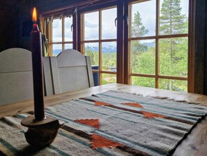 A room with a table, a candle, and a view of a forest through large windows. - Traditional cabin with views over Setesdalen (Bykle)