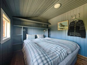 Une chambre à coucher avec un lit, une fenêtre, un porte-manteau et un tableau accroché au mur.