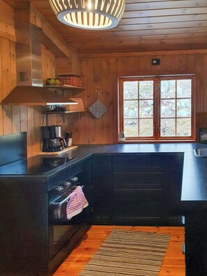 A kitchen with wooden cabinets, a stove, a coffee maker, and a window with a view of trees. - Traditional cabin with views over Setesdalen (Bykle)