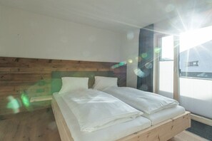 Ein Schlafzimmer mit einem hölzernen Kopfteil, einem Doppelbett mit weißer Bettwäsche und Blick ins Freie durch ein großes Fenster.