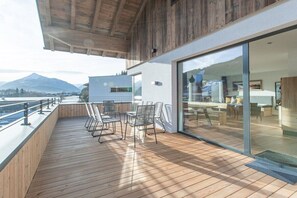 Eine moderne Terrasse im Freien mit Holzboden, Metallstühlen und einer Glastür, die zu einem Innenbereich führt.