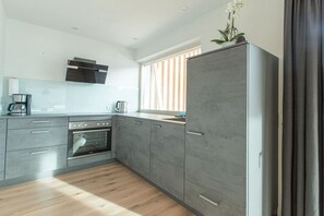 Eine moderne Küche mit grauen Schränken, einem Einbauofen und einem Fenster mit Jalousien.