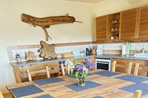 A wooden dining table with a vase of flowers, a wooden sign on the wall, and wooden cabinets in a kitchen. - Holiday apartment on the edge of the Harz Mountains (Ballenstedt\/ OT Rieder)