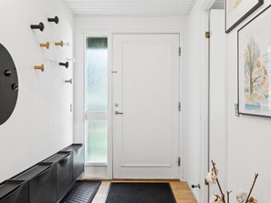 Ein Flur mit einer weißen Tür, einer schwarzen Fußmatte am Eingang und einem an der Wand befestigten Kleiderhaken mit verschiedenen Gegenständen.