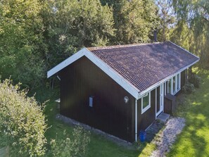 Ett envåningshus byggt av trä med ett sadeltak, omgivet av tät grönska.