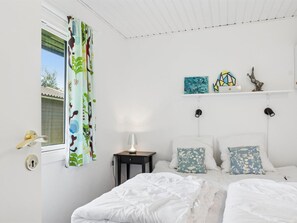 Ett sovrum med en säng, två sängbord, ett litet bord, ett fönster med gardin och konstverk som hänger på väggen.