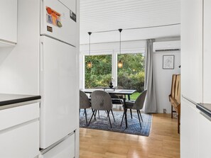 Ett modernt kök med vita skåp, en matplats med bord och stolar samt utsikt över grönområden utanför.