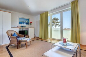 Une pièce avec un fauteuil en osier, une petite table, un téléviseur et une fenêtre avec des rideaux.