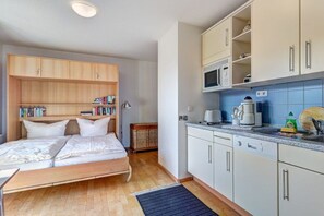 A compact bedroom with a bed, bedside tables, and a bookshelf. Adjacent is a kitchenette with a microwave, coffee maker, and cabinets. - 12 in the Marinar forum (Seebad Heringsdorf)