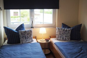 Hotellihuone, jossa on kaksi sänkyä, ikkuna, josta on näkymä, pieni pöytä lampun kanssa ja koriste-esine ikkunalaudalla.