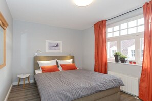 A bedroom with a bed, a bedside table, a window with curtains, and a radiator. - Villa La Mer - No. 13 (Kühlungsborn)