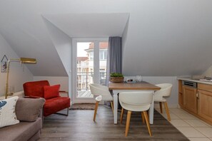 A compact living space with a dining area, a red chair, a sofa, and a kitchen area. - Villa La Mer - No. 13 (Kühlungsborn)
