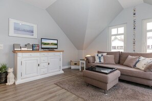 A modern living room with a white cabinet, a beige sofa, a coffee table, and a television on a wooden stand. - Villa La Mer - No. 13 (Kühlungsborn)
