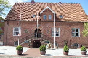 A brick building with a tiled roof, a central entrance with a staircase, and potted plants in front. - Holiday home with 3 bedrooms (Otterndorf)
