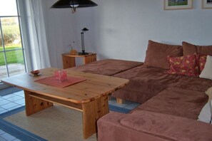 A room with a wooden table, a brown sofa, a small wooden side table, and a lamp. - Holiday home with 3 bedrooms (Otterndorf)