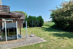 A backyard with a swing set, a covered play area, and a brick house. - Holiday home with 3 bedrooms (Otterndorf)
