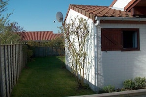 A white building with a red-tiled roof, a satellite dish, and a wooden fence. - Holiday home in Bredene with swimming pool (Bredene)