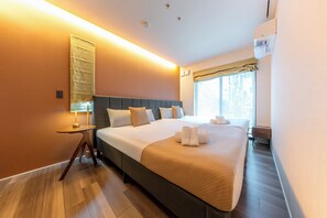 Una habitación de hotel moderna con una cama grande, una mesita de noche, una lámpara y una ventana con cortinas.