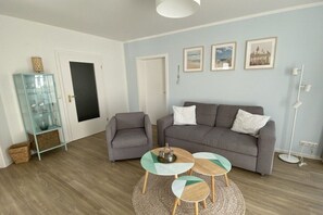 A living room with a grey sofa, two armchairs, and a coffee table with a tray. There are framed pictures on the wall and a floor lamp. - Holiday apartment "Am Ostseedeich" (Zingst)