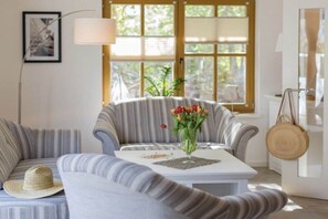 Ein Wohnzimmer mit gestreiften Sofas, einem weißen Couchtisch mit Blumenvase und einem großen Fenster mit Jalousien.