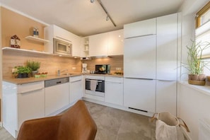 A modern kitchen with white cabinetry, a microwave, an oven, and a sink. - Holiday home with 2 bedrooms (Ostseebad Dierhagen)