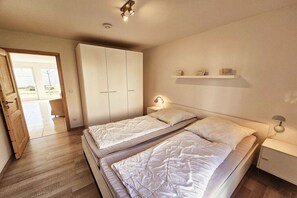 Een slaapkamer met twee bedden, een kast, een nachtkastje en een plank met decoratieve spullen.