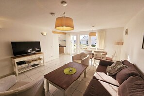 Ein Wohnzimmer mit Flachbildfernseher, Couchtisch aus Holz, braunem Sofa und einem Essbereich mit Tisch und Stühlen.