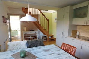 A kitchen with white cabinets, a wooden staircase, and a dining area with a table and chairs. - Holiday home with 2 bedrooms (Schönwalde am Bungsberg)