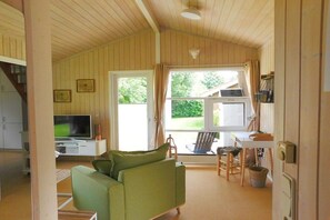 A cozy living room with a green sofa, a television, and a dining area with a table and chairs. - Holiday home with 2 bedrooms (Schönwalde am Bungsberg)