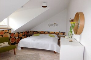 A bedroom with a sloped ceiling, a bed with white bedding, a green chair, a wooden headboard with a fruit pattern, and a wall-mounted mirror. - Holiday home with 2 bedrooms (Schönwalde am Bungsberg)