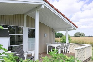 A covered outdoor area with a table and chairs, a window, and a view of a field. - Holiday home with 2 bedrooms (Schönwalde am Bungsberg)